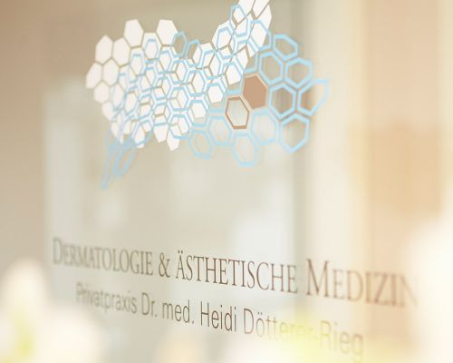 Abgebildet sind unscharfe Praxis-Symbole auf einer Glasvitrine in einer Frankfurter Privatpraxis für Dermatologie & ästhetische Medizin Dr. med. Dötterer-Rieg & Kollegen. Hautarzt García Cano arbeitet in dieser hautärztlichen Praxis in der Innenstadt.